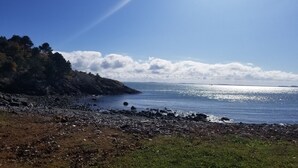 Uma costa rochosa com céu claro e reflexos de luz solar na água.