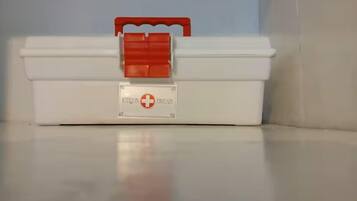 Un botiquín de primeros auxilios blanco con un asa roja y una etiqueta que dice 'BOTTQUIN FIRST AID'.