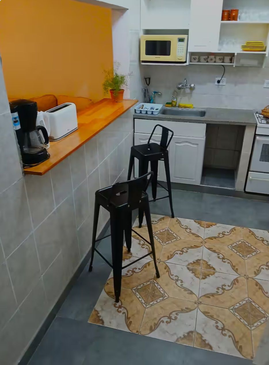 A compact kitchen with a microwave, toaster, sink, and two bar stools.