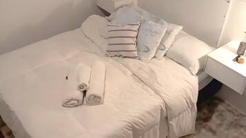 Un letto ben rifatto con un piumone bianco e cuscini, un comodino con una lampada e un tappeto morbido sul pavimento.