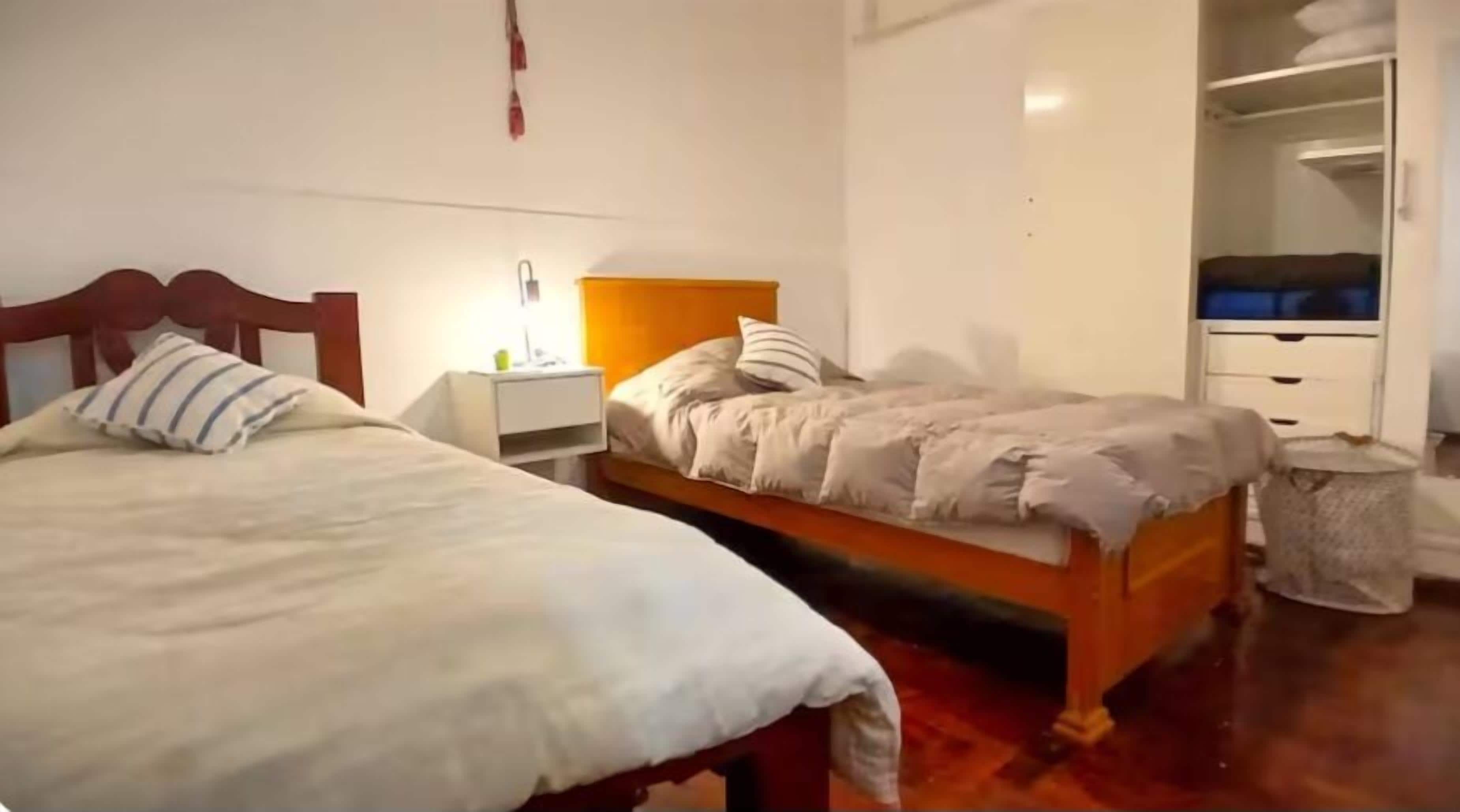 Un dormitori amb dos llits, una tauleta de nit, un armari i un safataire.