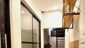 Un pasillo estrecho con un amplio ventanal corredera, un banco de madera y una escalera que sube a un nivel superior.