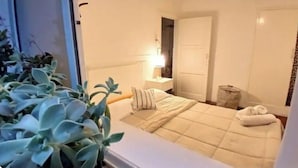 Un dormitorio con cama, mesita de noche, lámpara y una planta en maceta.