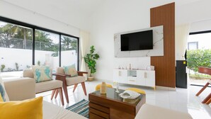 Un salon moderne avec un canapé, des fauteuils, une table basse, un téléviseur fixé au mur et une plante en pot.
