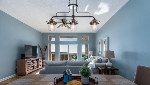 A living room with a large window, a sofa, a TV, and a dining table with a tray. - Summit Blue at TOPS'L , Gulf Views, Beach & Pool (Miramar Beach)