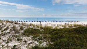A beach with a row of blue umbrellas and a wooden fence. - Summit Blue at TOPS'L , Gulf Views, Beach & Pool (Miramar Beach)