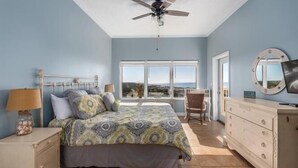 A bedroom with a bed, a dresser, a chair, a ceiling fan, and a large window with a view. - Summit Blue at TOPS'L , Gulf Views, Beach & Pool (Miramar Beach)