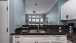 A kitchen with granite countertops, white cabinets, a double sink, and a ceiling fan. - Summit Blue at TOPS'L , Gulf Views, Beach & Pool (Miramar Beach)