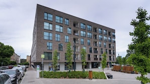Un edificio moderno a più piani con facciata in mattoni, ampie finestre e un'area di parcheggio con posti delimitati.