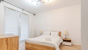 Una camera da letto moderna con un letto in legno, biancheria bianca, un comodino con una lampada e un termosifone.