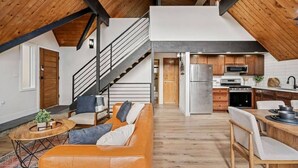 Um loft espaçoso com pé direito alto, cozinha com eletrodomésticos modernos, área de refeições e escada para um andar superior.