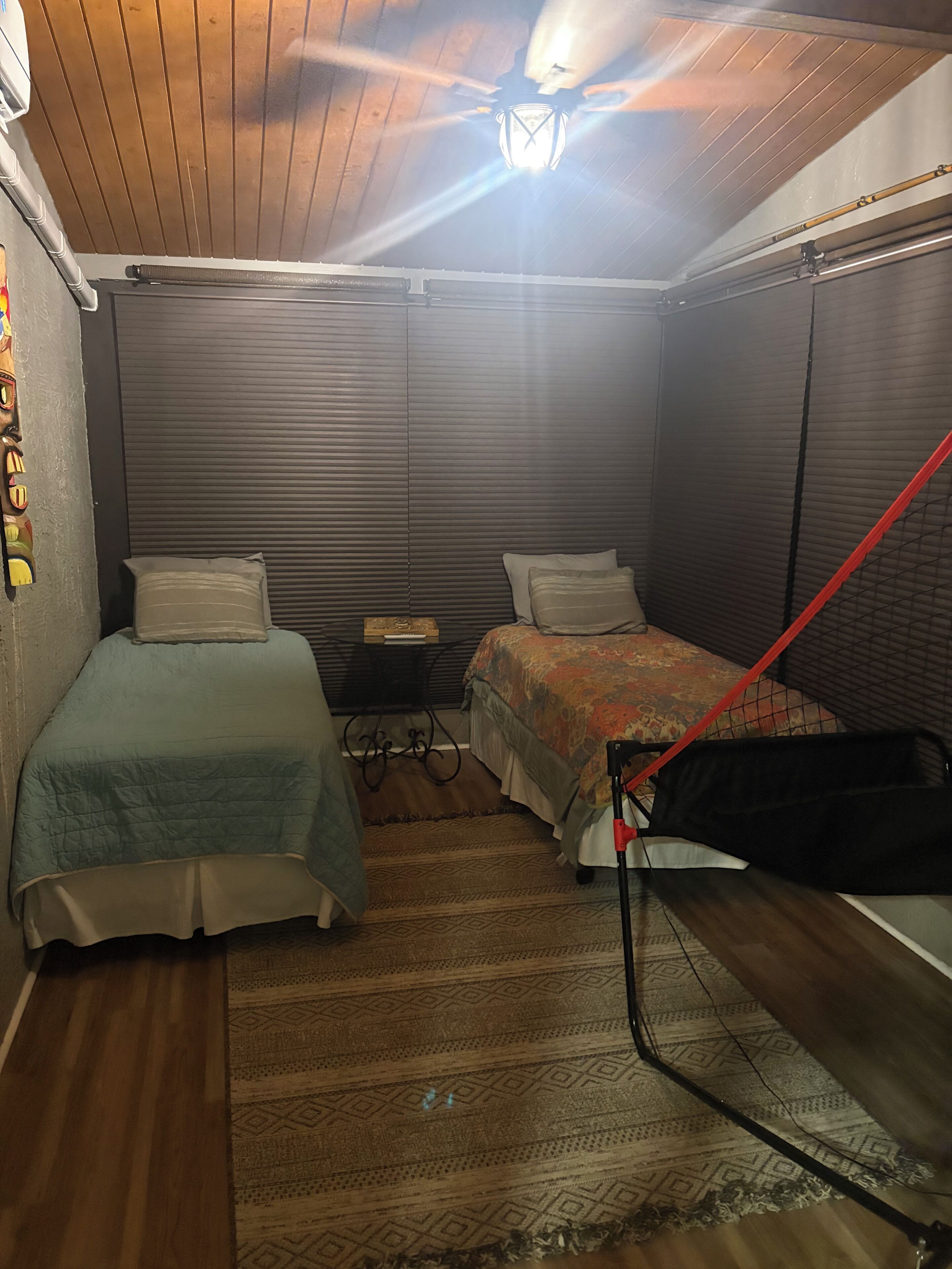 A small, dimly lit room with two beds, a ceiling fan, and a red safety railing.