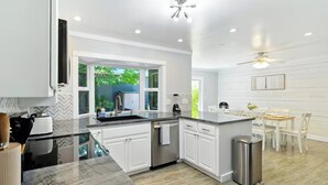 Una cocina moderna con armarios blancos, encimera de mármol y vistas al exterior con vegetación.