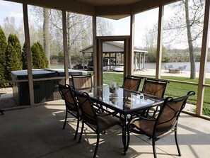 Eine überdachte Terrasse mit einem Glastisch und Stühlen, die auf einen Garten mit Grill und Gartenmöbeln blickt.