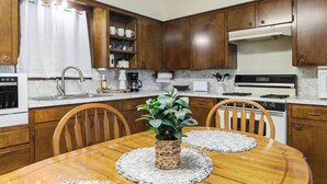A kitchen with wooden cabinets, a stove, a sink, and a dining table with chairs. - The Rose 1 (Broussard)