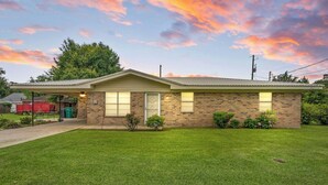 A single-story brick house with a covered porch, a front yard, and a red truck in the background. - The Rose 1 (Broussard)