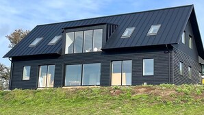 Una casa moderna de dos pisos con fachada oscura, ventanas grandes y techo inclinado.