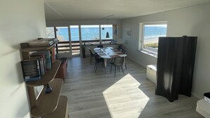 Ett rymligt rum med ett stort bord, stolar, en bokhylla och utsikt över havet genom stora fönster.