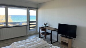 Ett sovrum med en säng, ett skrivbord med en stol, en tv och utsikt över havet genom ett fönster.