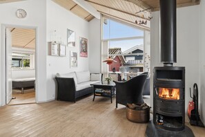 Ein gemütliches Wohnzimmer mit Kamin, einer Couch, einem Couchtisch und Blick ins Freie.