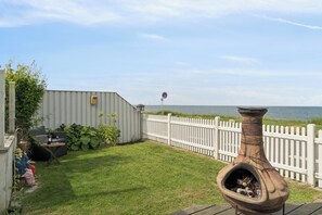 A backyard with a white fence, a barbecue grill, and a view of the water.