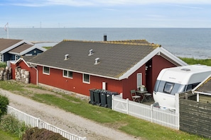 Ein rotes Haus mit weißem Zaun, einem weißen Wohnmobil und Blick auf das Meer und eine Brücke.