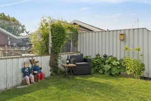 A fenced backyard with a wicker sofa, a small table, and two garden statues. - Lovely holiday home panoramic view over the sea (Slagelse)