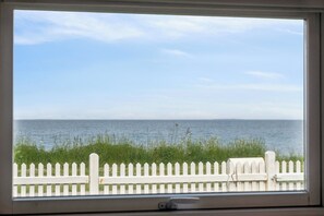 A view through a window of a white picket fence, a grassy area, and a calm body of water. - Lovely holiday home panoramic view over the sea (Slagelse)