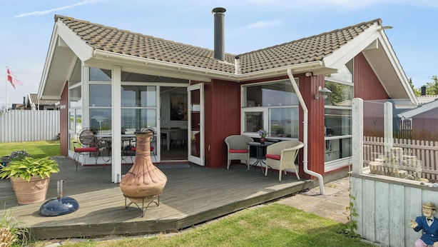 A house with a deck, a chimney, and a dining area with chairs and a table. - Lovely holiday home panoramic view over the sea (Slagelse)