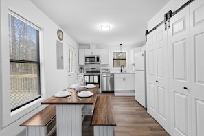 A modern kitchen with white cabinets, stainless steel appliances, and a wooden dining table set for four. - 8 Minutes to UNC - Outdoor Deck - Washer and Dryer (Chapel Hill)