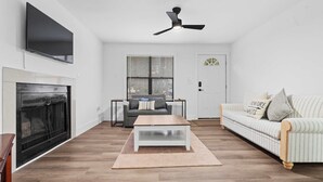 A living room with a fireplace, a television mounted on the wall, a ceiling fan, a sofa, and a coffee table. - Minutes From UNC - 15 Min to Duke - Private Deck (Chapel Hill)
