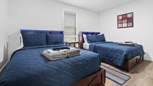 A bedroom with two beds, a window with blinds, a wall-mounted artwork, and a wooden floor. - Minutes From UNC - 15 Min to Duke - Private Deck (Chapel Hill)