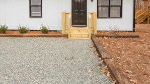 A single-story building with a black door and windows, a gravel driveway, and a wooden deck. - Minutes From UNC - 15 Min to Duke - Private Deck (Chapel Hill)
