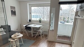 A modern kitchen with wooden flooring, a dining area with a white table and chairs, and a glass partition separating the kitchen from the living area. - FeWo am Deich 2, modern apartment with balcony and elevator (Bremerhaven)