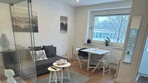 A modern living room with a glass partition, a grey sofa, a dining table with chairs, and a large window providing a view of the outside. - FeWo am Deich 2, modern apartment with balcony and elevator (Bremerhaven)