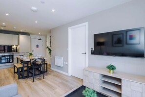 A modern kitchen with built-in appliances, a dining area with a table set for two, and a large flat-screen TV mounted on the wall. - Luxury Liverpool Apartment: 2BR, Free Street Parking & City Center (Liverpool)