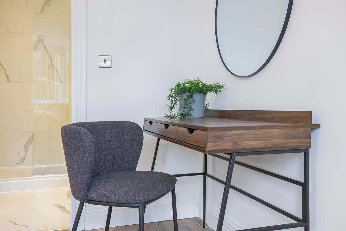 Un escritorio moderno con una silla gris, una pequeña planta en maceta y un espejo instalado en la pared.