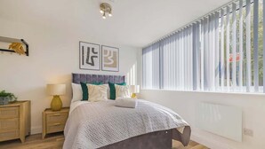 Un dormitorio moderno con una cama grande, una mesita de noche con lámpara y una ventana con persianas.