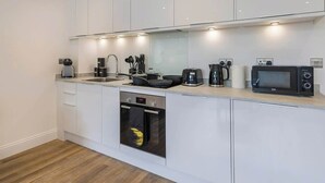 Una cocina moderna con armarios blancos, horno empotrado, microondas y cafetera.