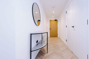 A hallway with a wooden door at the end, a mirror on the wall, and a glass table with a marble-like surface. - Stylish 2 Bed 2 Bath in Central Manchester (Manchester)