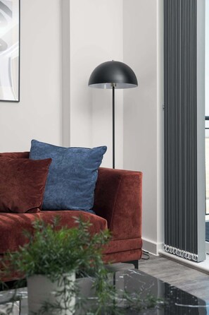 A modern living room with a red sofa, a blue pillow, and a black floor lamp. - Lovely Home Near Canal, Park, & Central MK (Milton Keynes)