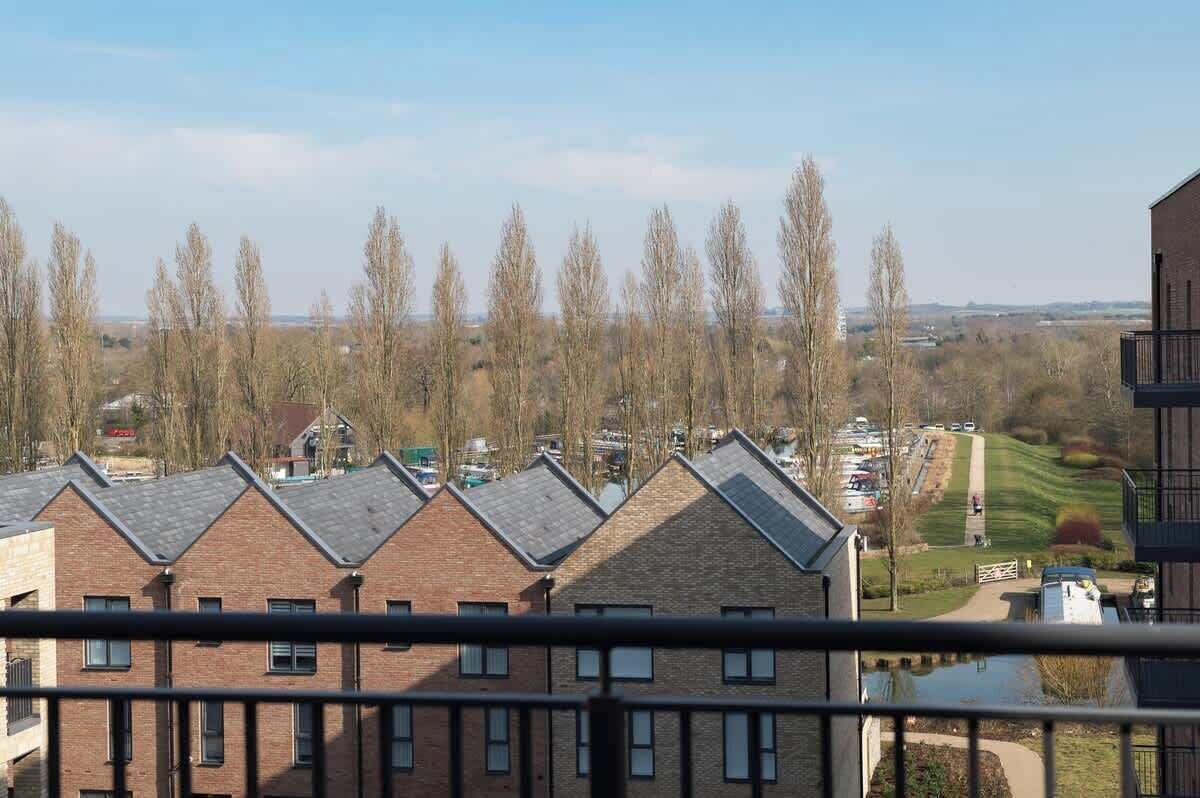 A residential area with multiple brick houses, a clear sky, and a distant view of a park with a pathway.