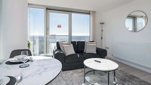 Ein modernes Wohnzimmer mit großem Fenster, einem runden Spiegel, einem grauen Sofa und einem Marmortisch.
