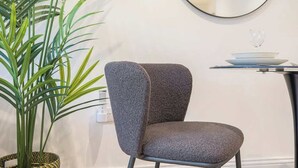 Una cadira moderna amb teixit texturat, un mirall rodó a la paret i una planta en test.