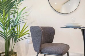A modern chair with a textured fabric, a round mirror on the wall, and a potted plant. - Central Gravesend 1BR | Kitchen +Wi-Fi | Sleeps 2 (Gravesend)