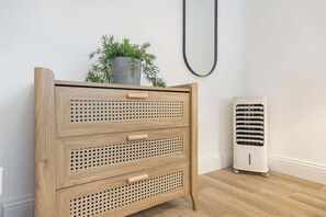 A wooden dresser with three drawers and a potted plant on top. A white portable heater is next to it. - Central Gravesend 1BR | Kitchen +Wi-Fi | Sleeps 2 (Gravesend)