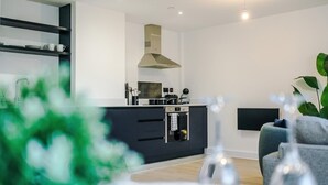 A modern kitchen with dark cabinetry, a stainless steel range hood, and a built-in oven. - Stylish Manchester Apartment: City Access & Wi-Fi (Manchester)