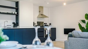 A modern kitchen with dark cabinetry, a central island, and a built-in stove. - Stylish Manchester Apartment: City Access & Wi-Fi (Manchester)