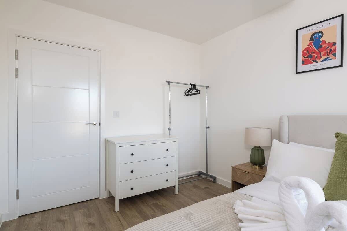 Una camera da letto con un letto, una cassettiera, un comodino, un appendiabiti e un quadro incorniciato al muro.