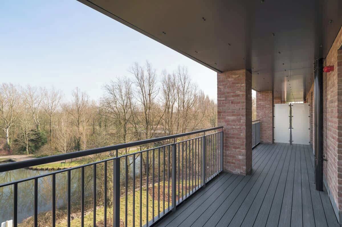 A balcony with a view of a lake and trees, featuring a wooden deck and metal railing.